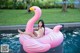 A woman sitting on an inflatable flamingo floating in a pool.