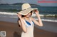 A woman in a white dress and a straw hat on the beach.