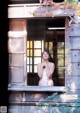 A naked woman standing in the window of a wooden house.