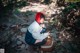 A woman with a red headscarf sitting on a rock in the woods.