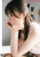 A young woman sitting on a bed with her hand on her chin.